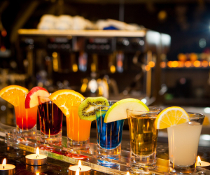 Side view cocktail shots with slice of lemon and kiwi slice and candles on bar background